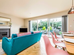 A modern living room with a teal sofa, pink chairs, a fireplace, and a TV.
