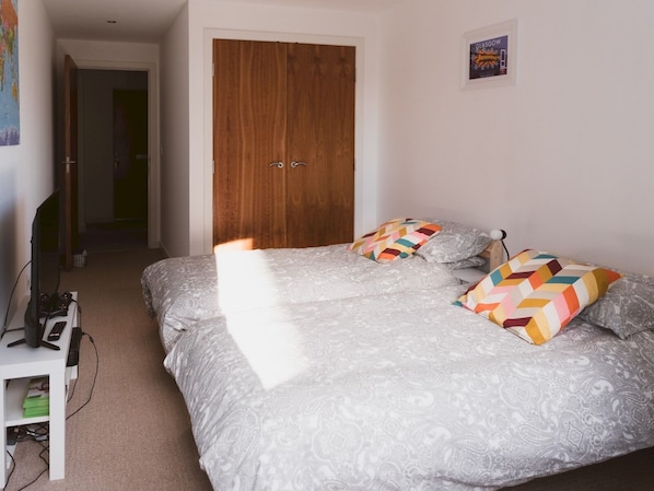 A bedroom with a double bed, a wooden wardrobe, a desk with a computer, and a poster on the wall.
