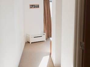 A narrow hallway with a white storage bench, a framed picture on the wall, and a window with brown curtains.