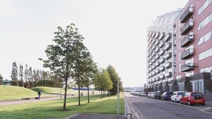 En moderne bygate med en række lejlighedskomplekser i rød mursten, en sti for gående og parkerede biler.