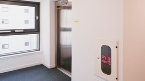 Et hotelværelse med et stort vindue, en dør med skilt 'Dry Riser' og et tæppe belagt gulv.