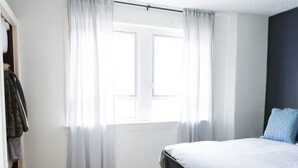 A bedroom with a bed, a window with curtains, a wooden floor, and a wardrobe.