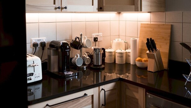 A modern kitchen with wooden cabinets, a black countertop, and various appliances including a coffee maker, toaster, and kettle.