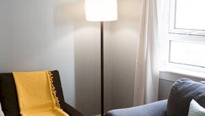 A room with a floor lamp, a chair with a yellow throw, and a window with curtains.