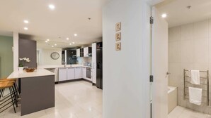 Une cuisine moderne dotée d’un îlot central, d’appareils électroménagers intégrés et donnant sur la salle de bain adjacente.