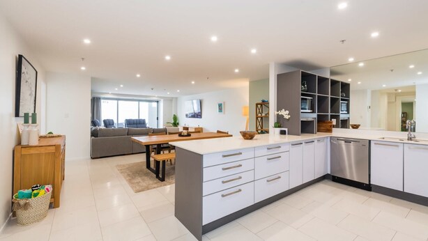 Une cuisine moderne dotée d’un îlot central, de meubles blancs et d’appareils électroménagers intégrés.
