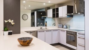 Une cuisine moderne avec des armoires blanches, des appareils en acier inoxydable, un grand miroir et un saladier en bois posé sur le comptoir.