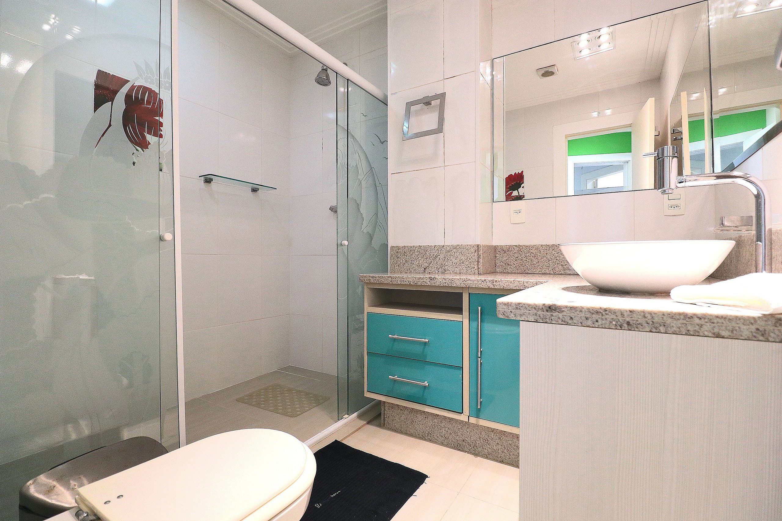 A bathroom with a glass shower enclosure, a white sink, teal cabinets, and a mirror.