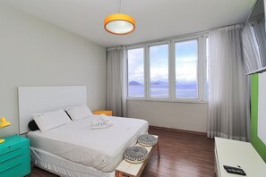A bedroom with a bed, bedside table, lamp, and a view of the sea. - Rio Spot Homes T037 Ocean View (Rio de Janeiro)