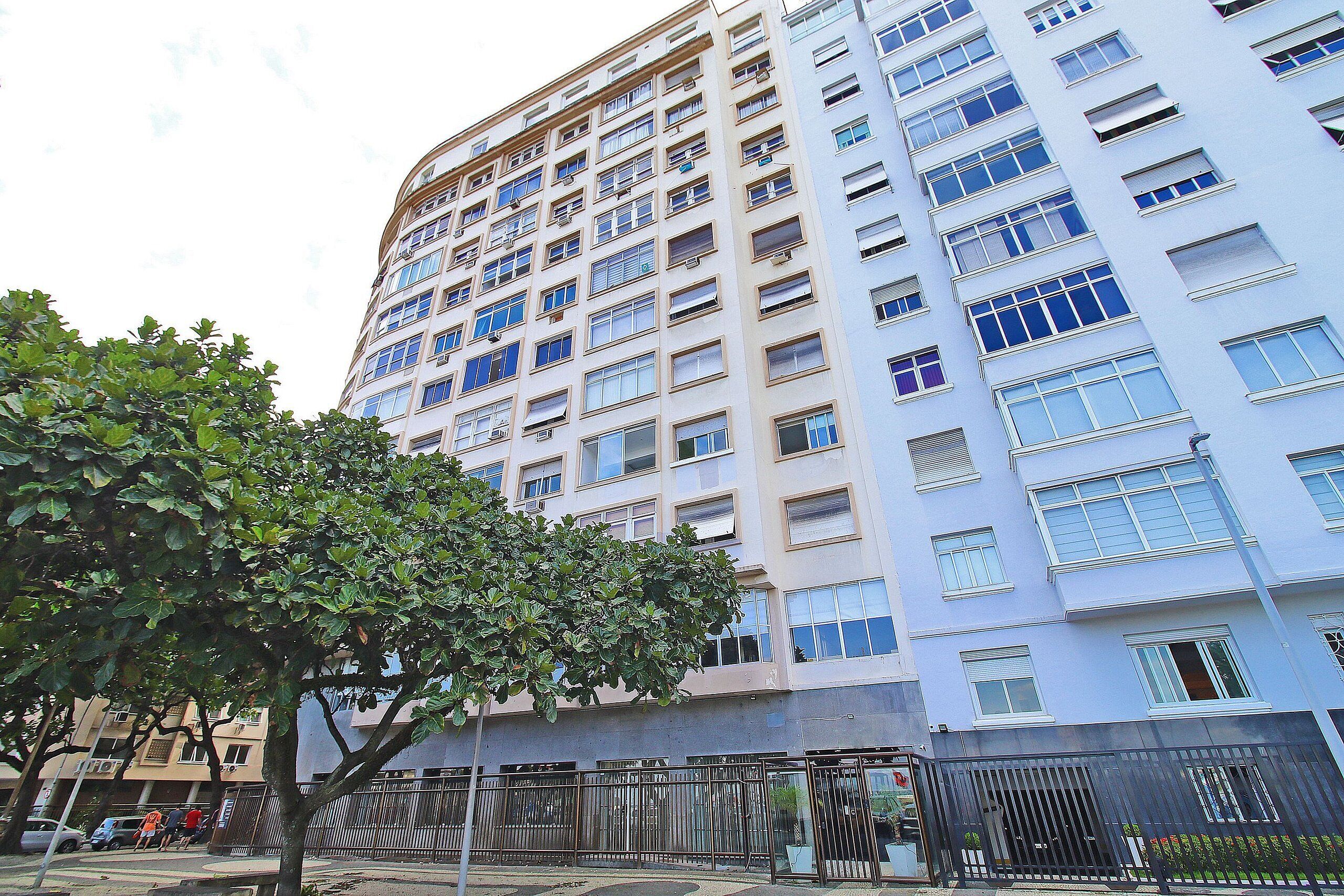 A multi-story residential building with a uniform facade, large windows, and a tree in the foreground.