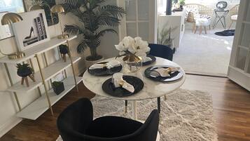 A dining area with a round table set for four, a black chair in the foreground, and a potted plant in the background.