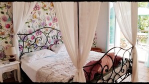 A bed with a canopy, a bedside table with a lamp, and a floral wallpaper. - Secluded private villa with pool close to the mountains, just 25 mins from Nice (Coaraze)