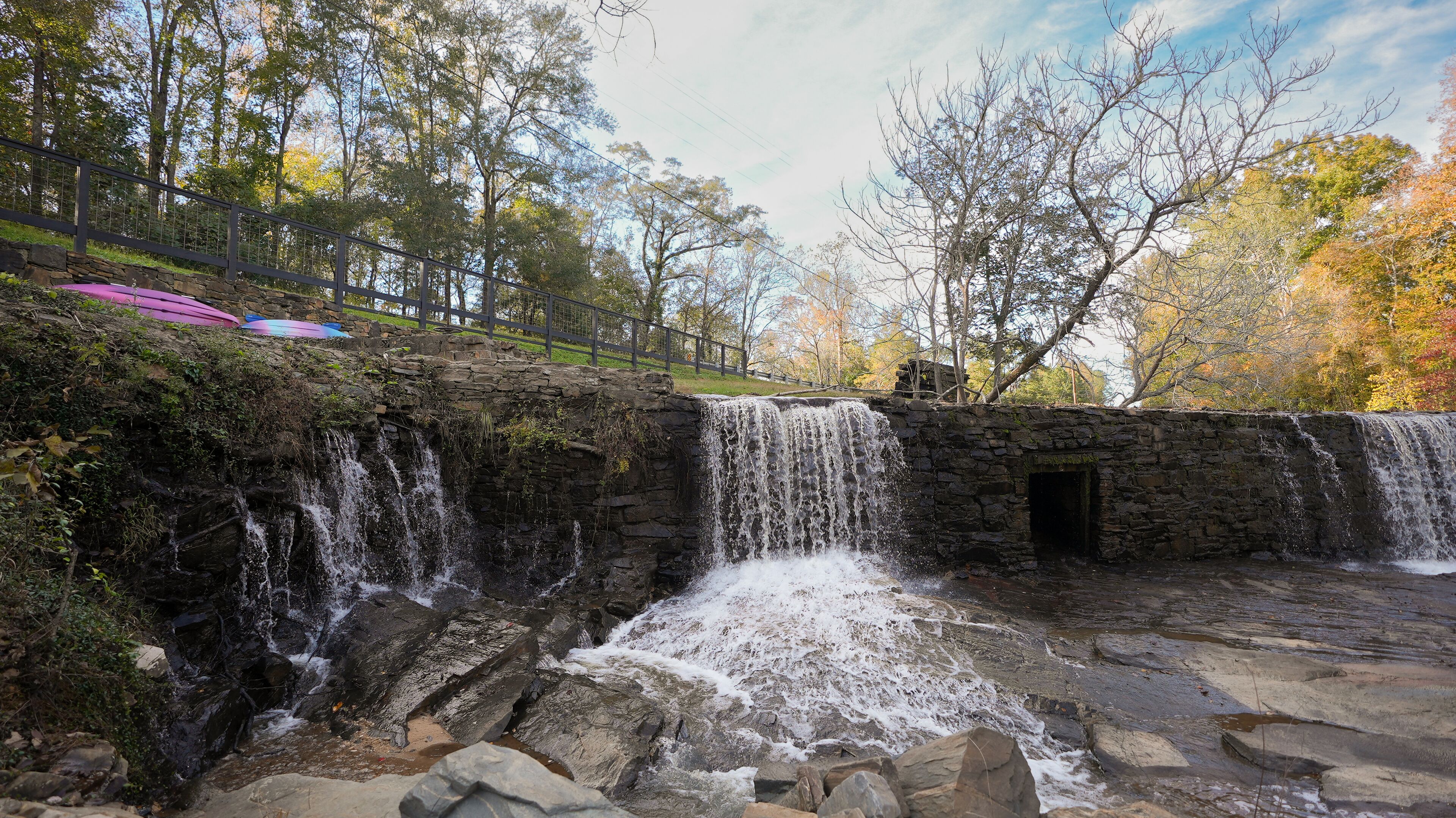Une cascade artificielle en pierre, avec une petite entrée de grotte, entourée d’arbres et d’un mur de pierre.