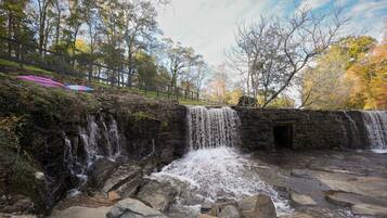 Une cascade artificielle en pierre, avec une petite entrée de grotte, entourée d’arbres et d’un mur de pierre.