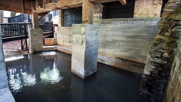 A rustic interior with stone walls, wooden beams, and a central water feature. - Meadows MIll House II (Salem)