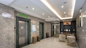 A modern hotel lobby with marble flooring, two elevators, and a reception area with a dark wood panel and framed artwork. - GreenTree Inn Express Hotel (Shanghai Songjiang Sports Center Subway Station) (Shanghai)