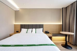 Hotellihuone, jossa on sänky, yöpöydät, pieni pyöreä pöytä ja penkki.