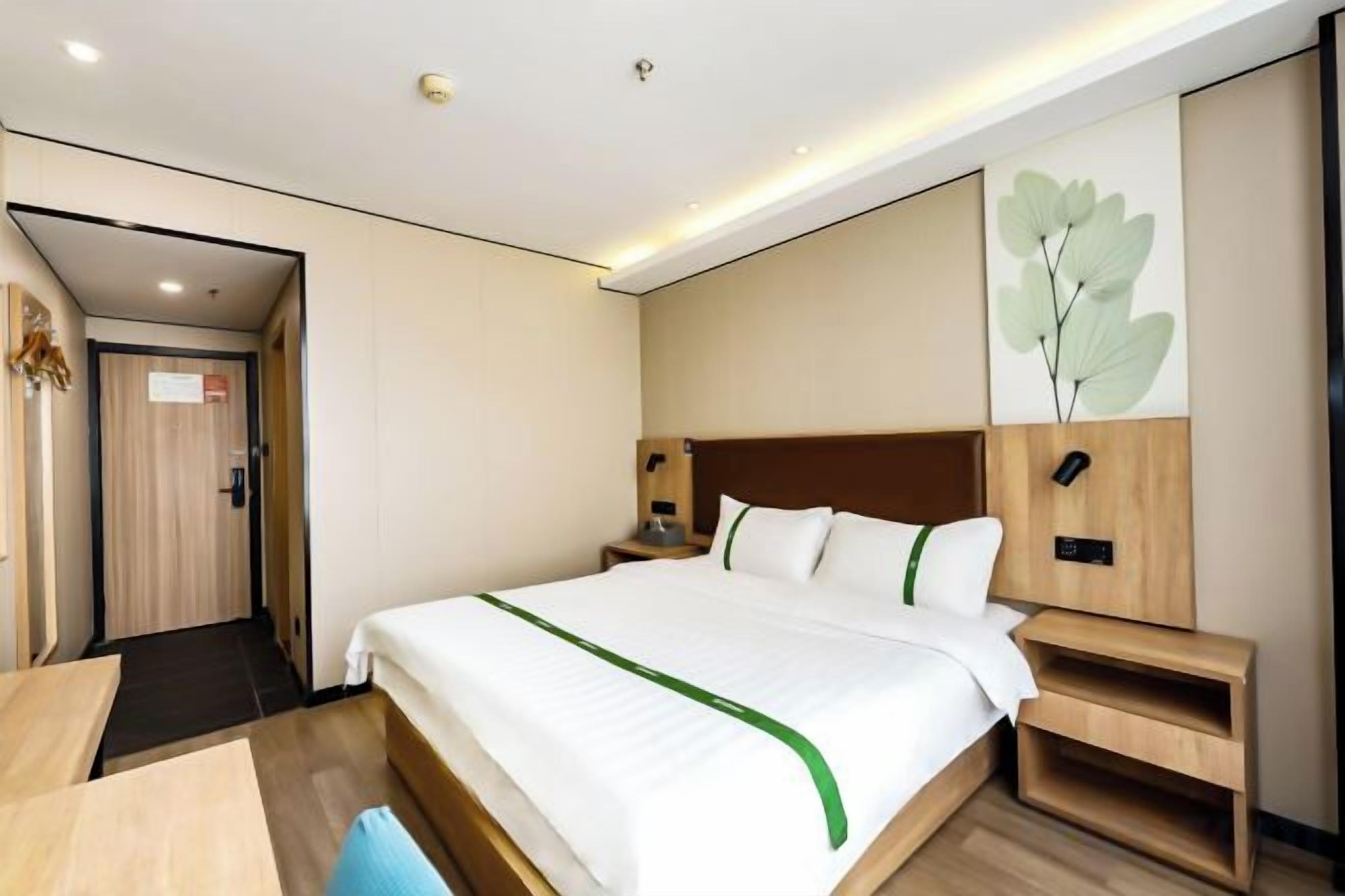 A hotel room with a bed, bedside tables, a desk, and a door.