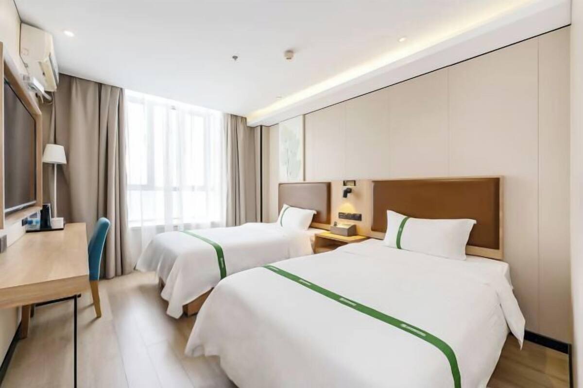 A hotel room with two beds, a desk, a chair, a lamp, and a window.