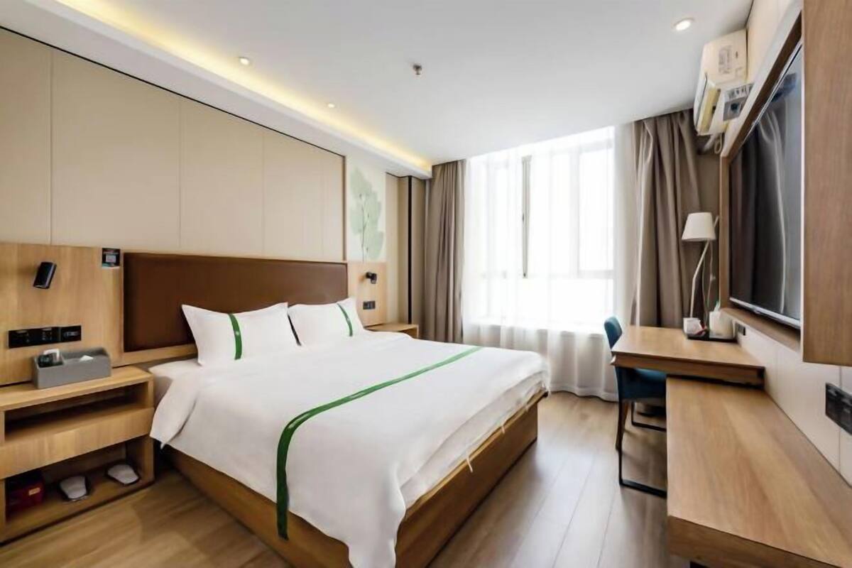 A hotel room with a bed, bedside table, lamp, and a desk with a chair.