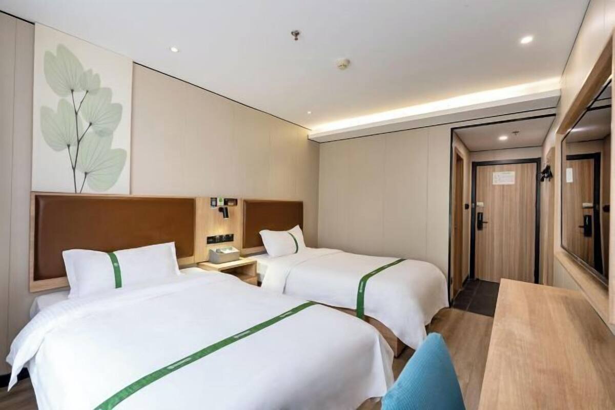 A hotel room with two beds, a wooden headboard, a bedside table, a mirror, and a wooden floor.