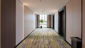 A hotel corridor with patterned flooring, a potted plant, and a view of the outside through a window. - GreenTree Inn Express Hotel (Shanghai Songjiang Sports Center Subway Station) (Shanghai)