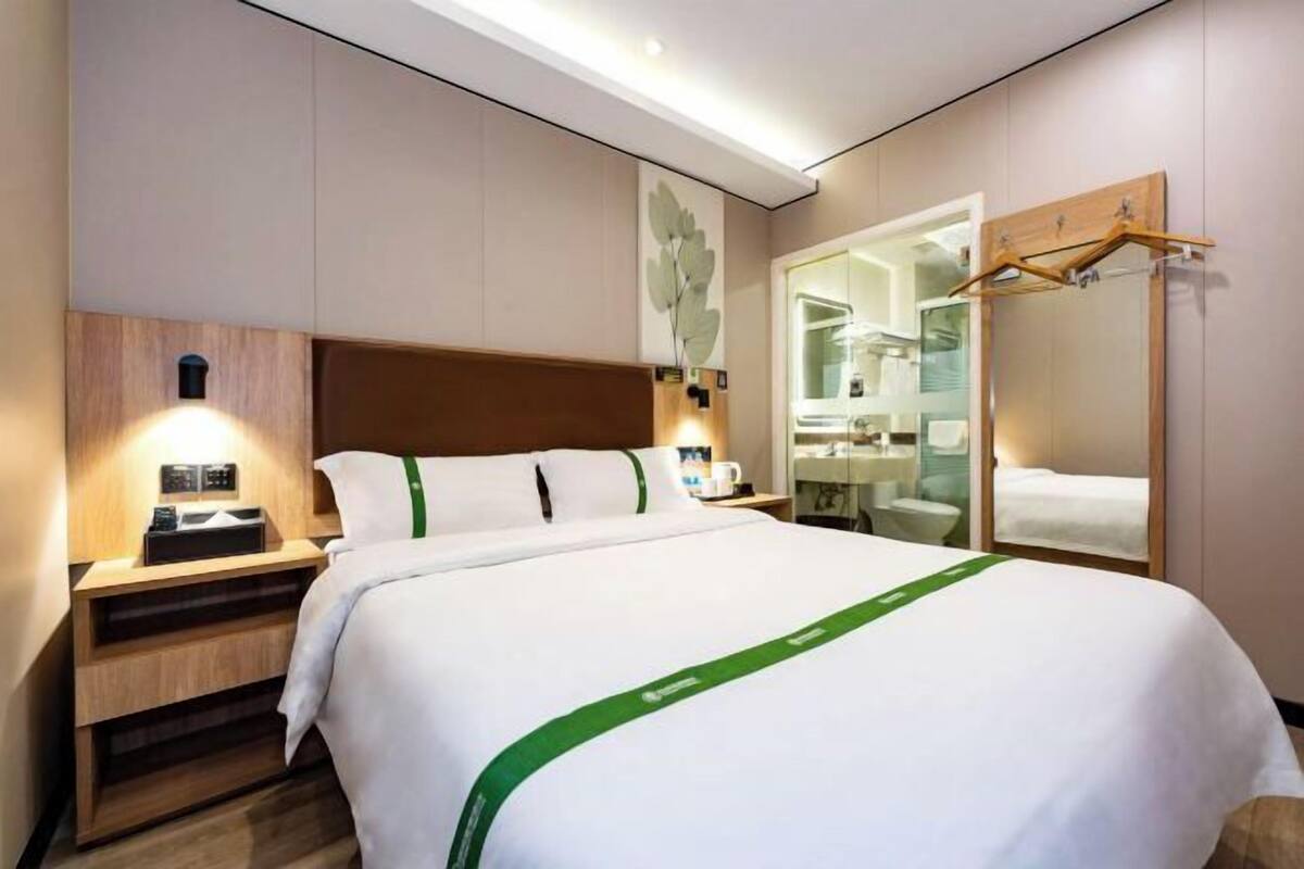 A hotel room with a bed, bedside tables, a mirror, and a wardrobe.