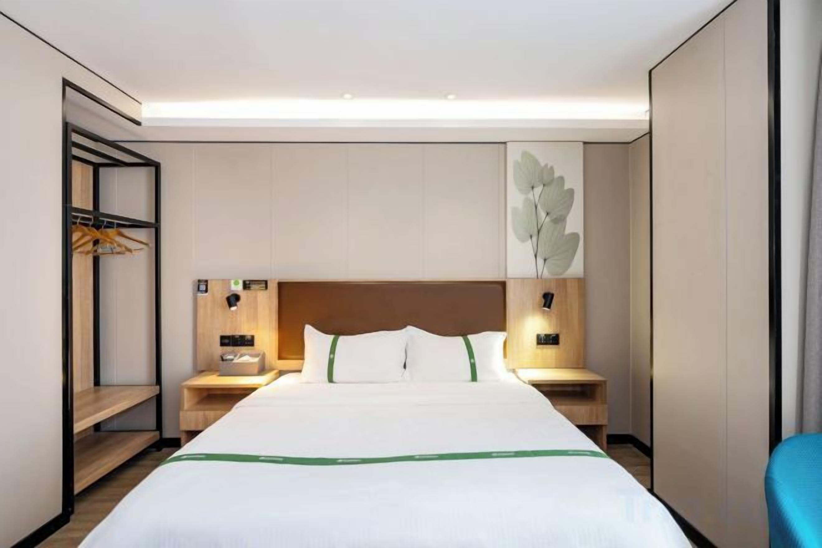 A hotel room with a large bed, bedside tables, a wardrobe, and a wall-mounted artwork.