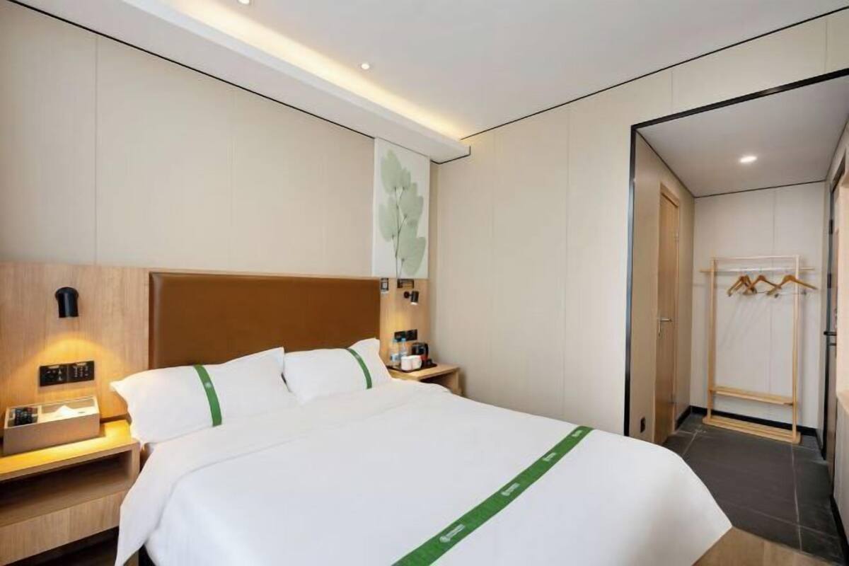 A hotel room with a bed, bedside table, lamp, and a wall-mounted artwork.