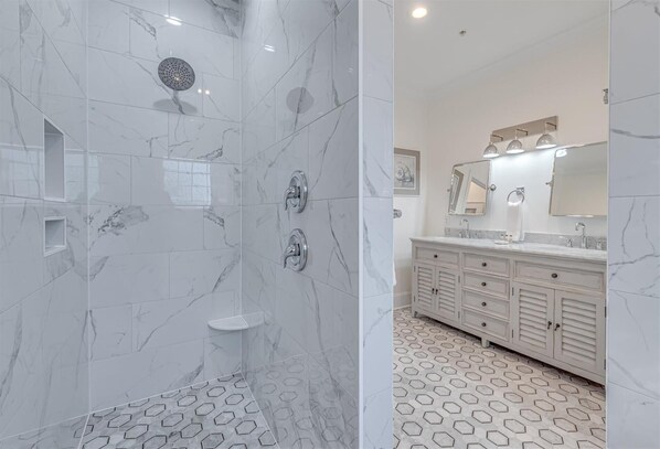 Un baño con ducha, tocador con espejo y suelo estampado.