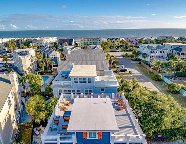 A coastal residential area with a prominent blue house featuring a rooftop deck with outdoor furniture.