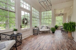 A sunroom with large windows, a brick floor, and a white sofa.