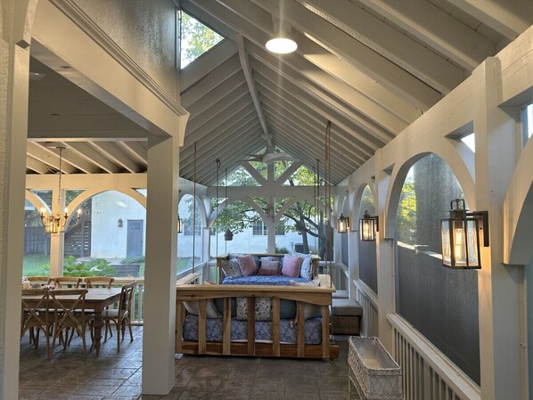 A covered patio with a wooden bench, a dining table, and chairs.