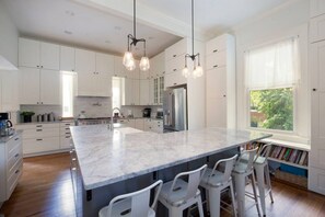 A modern kitchen with white cabinets, a large island with bar stools, and pendant lighting.