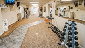 Un gimnasio con equipo de ejercicio, televisión y alfombra estampada.