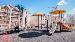 Un parque infantil con toboganes y estructuras para escalar, rodeado de edificios de varios pisos con balcones.