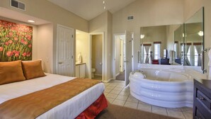 Una habitación de hotel con una cama grande, un jacuzzi, un baño con espejo y un cuadro en la pared.
