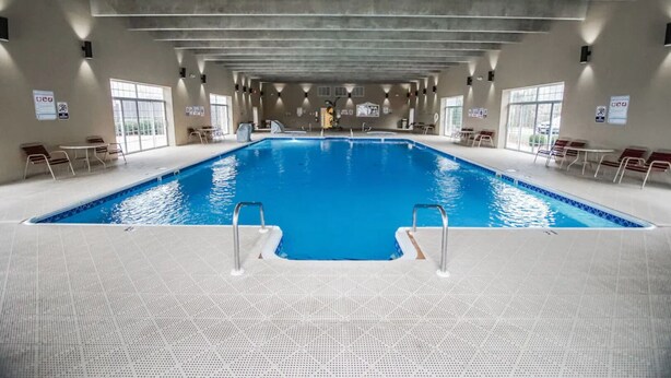Una piscina interior con agua cristalina, rodeada de sillones de descanso y un suelo de baldosas.