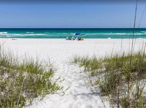 A beach path leading to a sandy area with a few umbrellas and beach chairs, under a clear sky.