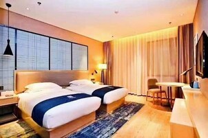 Habitación de hotel con dos camas, un escritorio, una silla, un televisor y un ventanal grande.