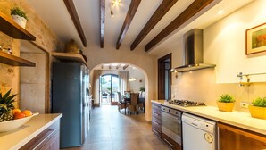 A modern kitchen with wooden beams, a dishwasher, a stove, and a dining area with a view. - Modern villa in Mallorca Pleta with swimming pool (Manacor)