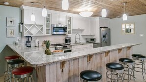 A kitchen with white cabinets, a large island with bar stools, a microwave, oven, and refrigerator. - Rustic Beach Front Home - 6 Bedrooms - Private Beach Access - Large Groups (Melbourne Beach)