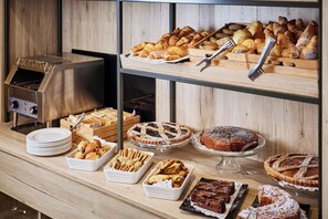 Monipuolinen buffet, jossa on tarjolla erilaisia leivonnaisia, kuten piirakoita ja muita makeita herkkuja, sekä grillipiste.