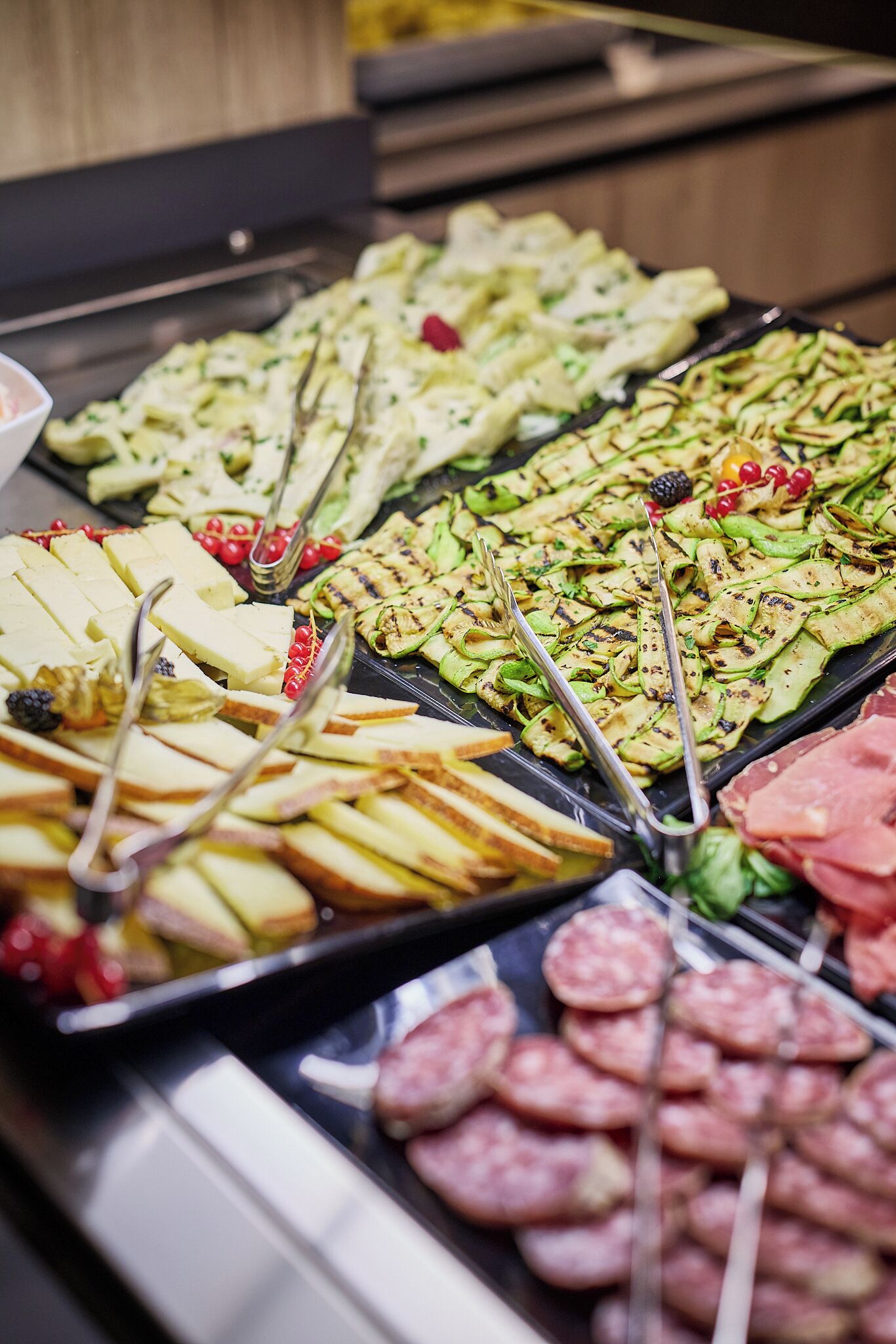 Un bufé con diferentes opciones de comida, entre ellas carnes frías, quesos y verduras.