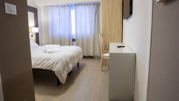 Ein Hotelzimmer mit Bett, Schreibtisch mit Stuhl, Fernseher und einem Fenster mit Vorhängen.