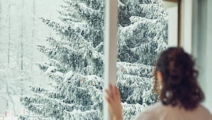 A person standing by a window with a view of snow-covered trees. - Hotel Hermitage (Sestriere)