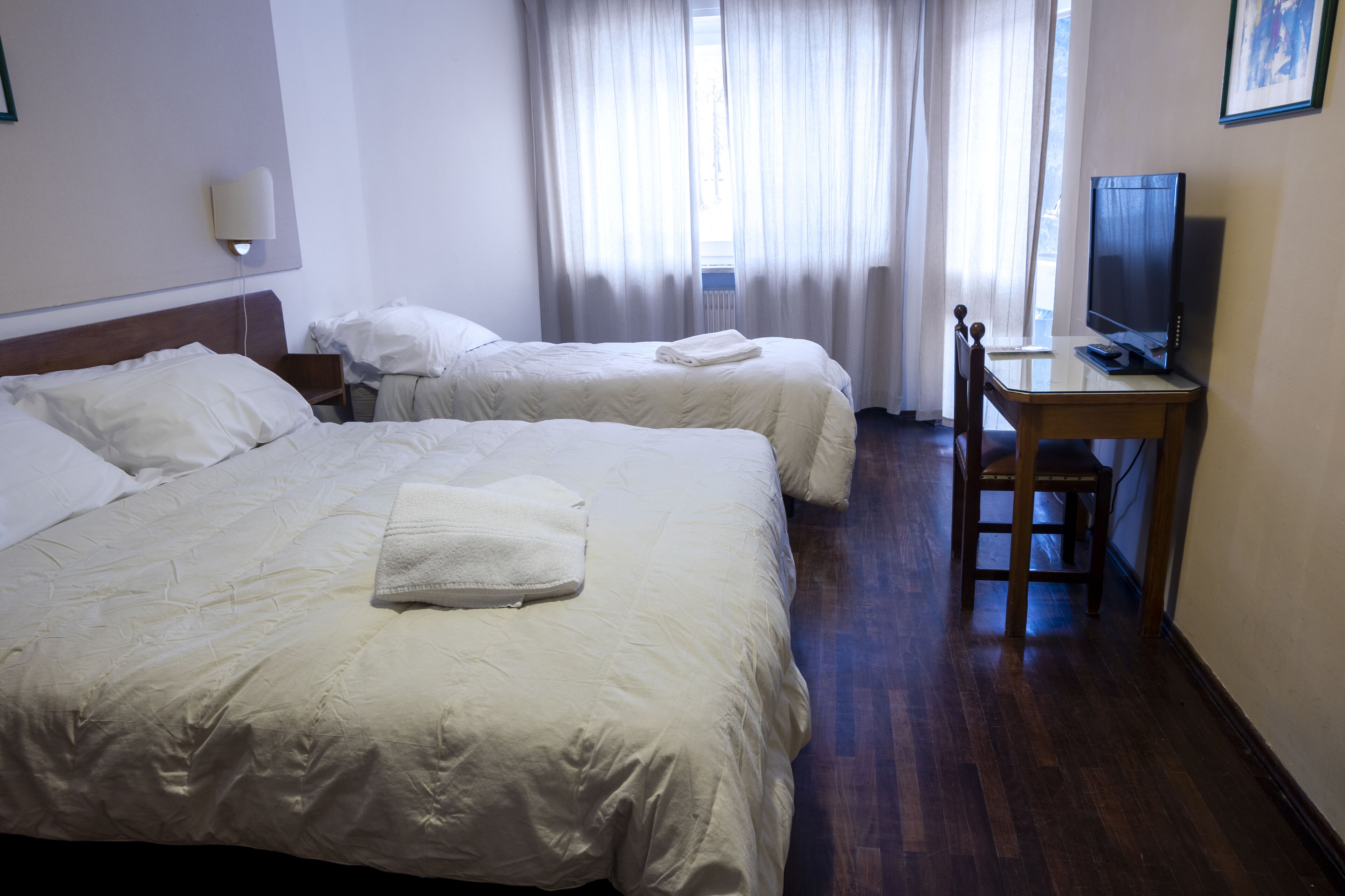 Een hotelkamer met twee bedden, een bureau met een televisie en een raam met gordijnen.