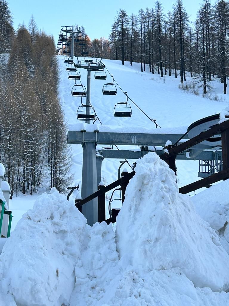 A ski lift with chairs ascending a snowy slope, surrounded by trees.