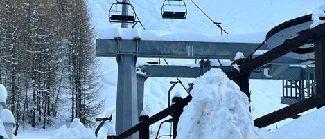 A ski lift with chairs ascending a snowy slope, surrounded by trees.