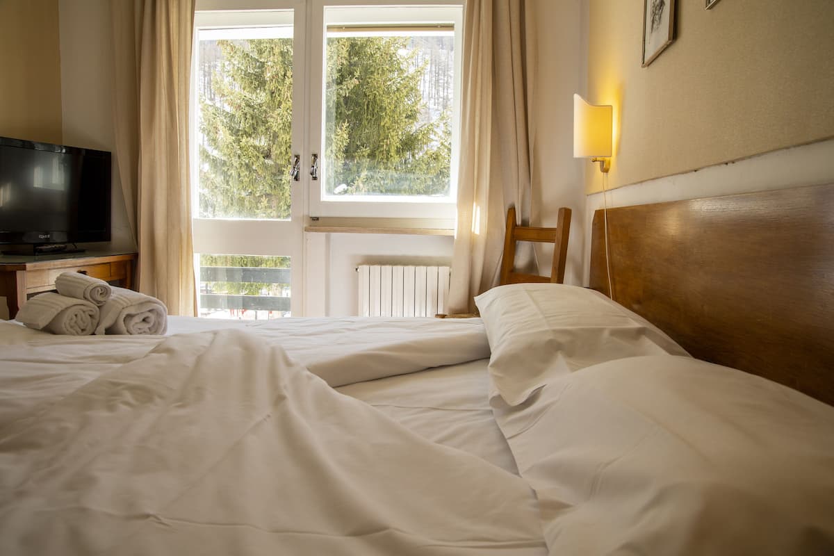 Une chambre d’hôtel avec un lit, une télévision, une chaise et une fenêtre avec des rideaux.